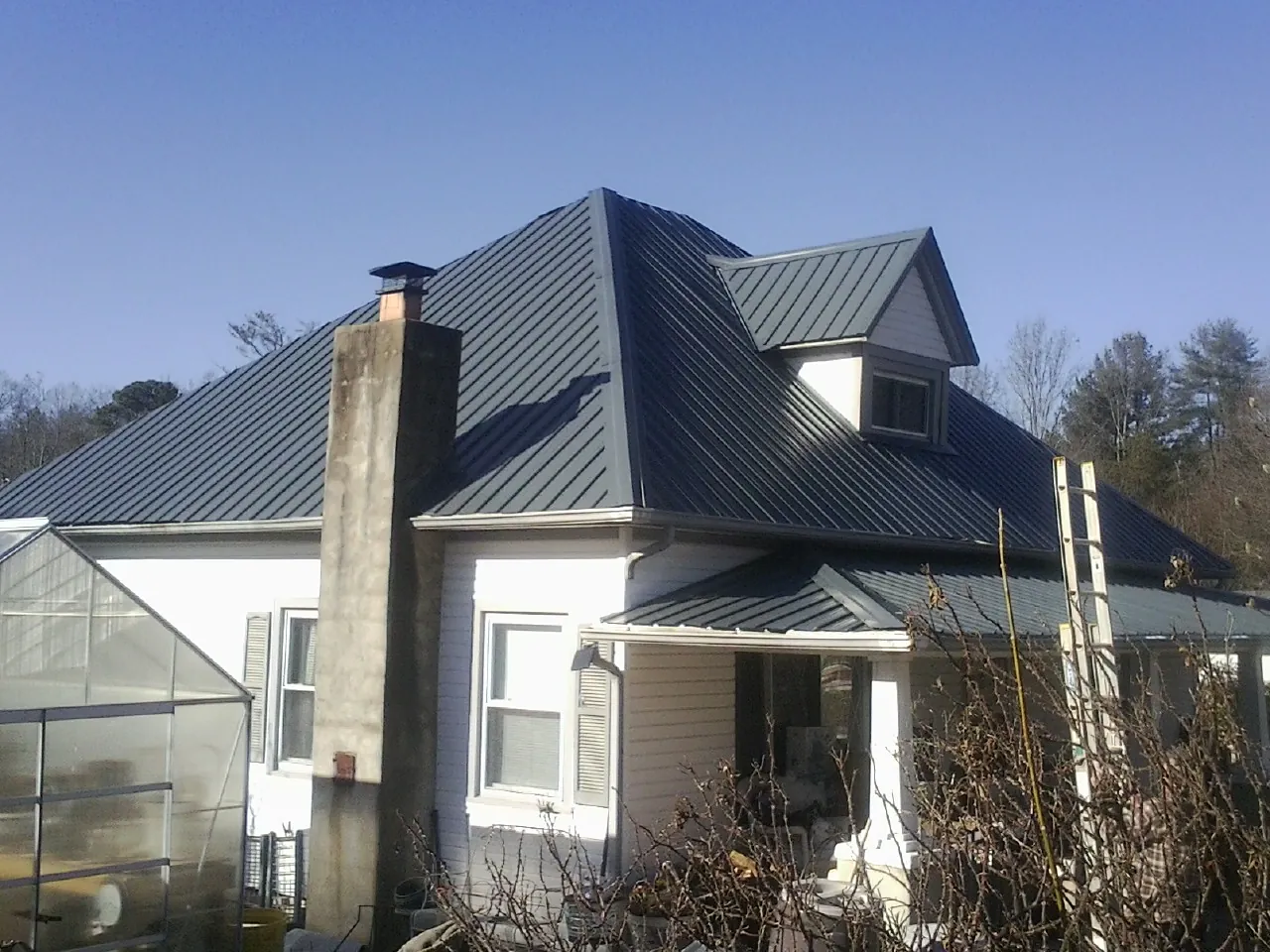 Dark blue standing seam metal roof on a white farmhouse with dormer — Slate & Tile Roof Repair by Roofing Brothers in Slayden