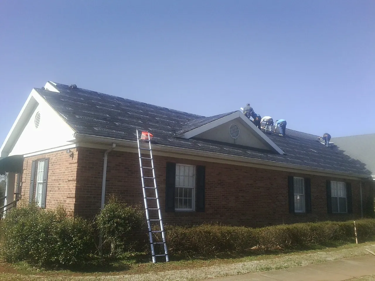 Crew tearing shingles off a brick ranch roof with a ladder set — Emergency Roof Repair work by our crew in Slayden