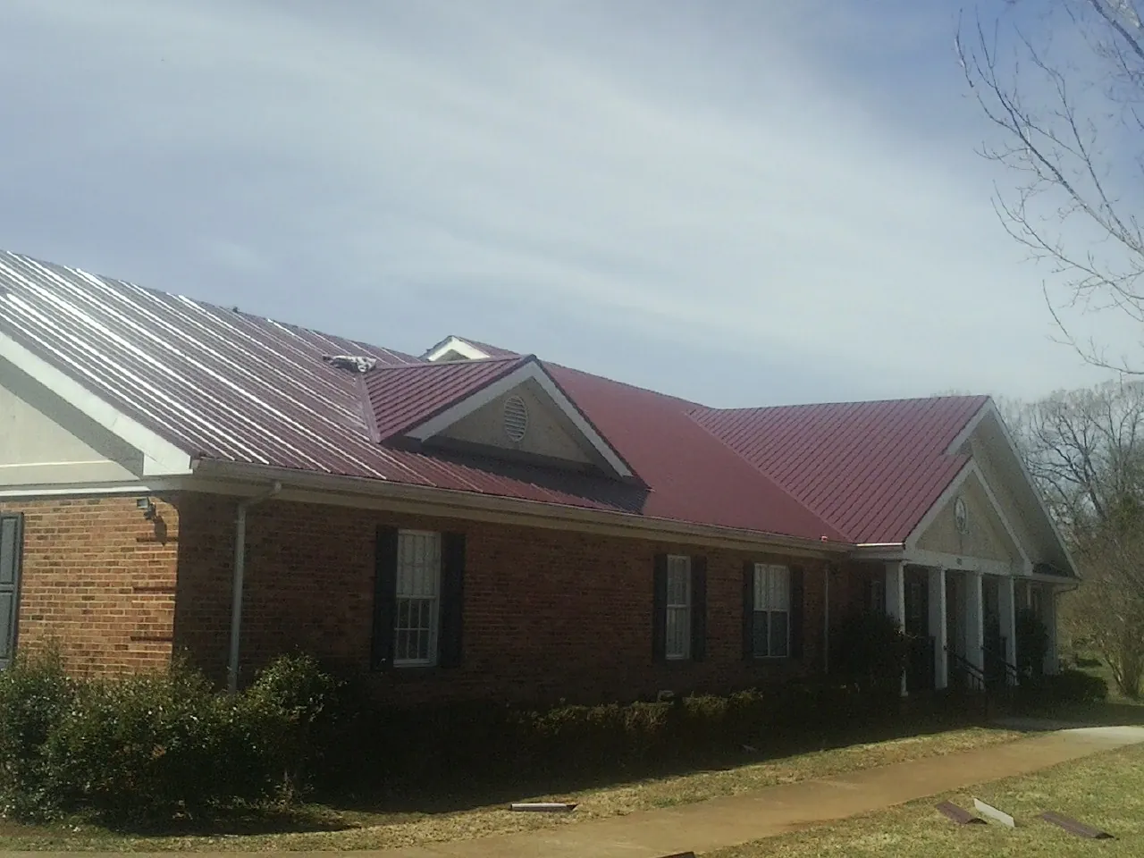Red metal roof with gabled entries on a long brick building, from a Hail Damage Roof Repair job in Slayden