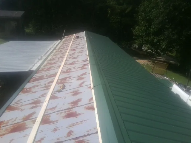 Old rusted panels beside newly installed green metal roofing — Wind Damage Roof Repair by Roofing Brothers in Slayden
