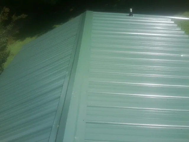 New green metal panels meeting at the ridge of a roof — Flat Roof Repair work by our crew in Slayden