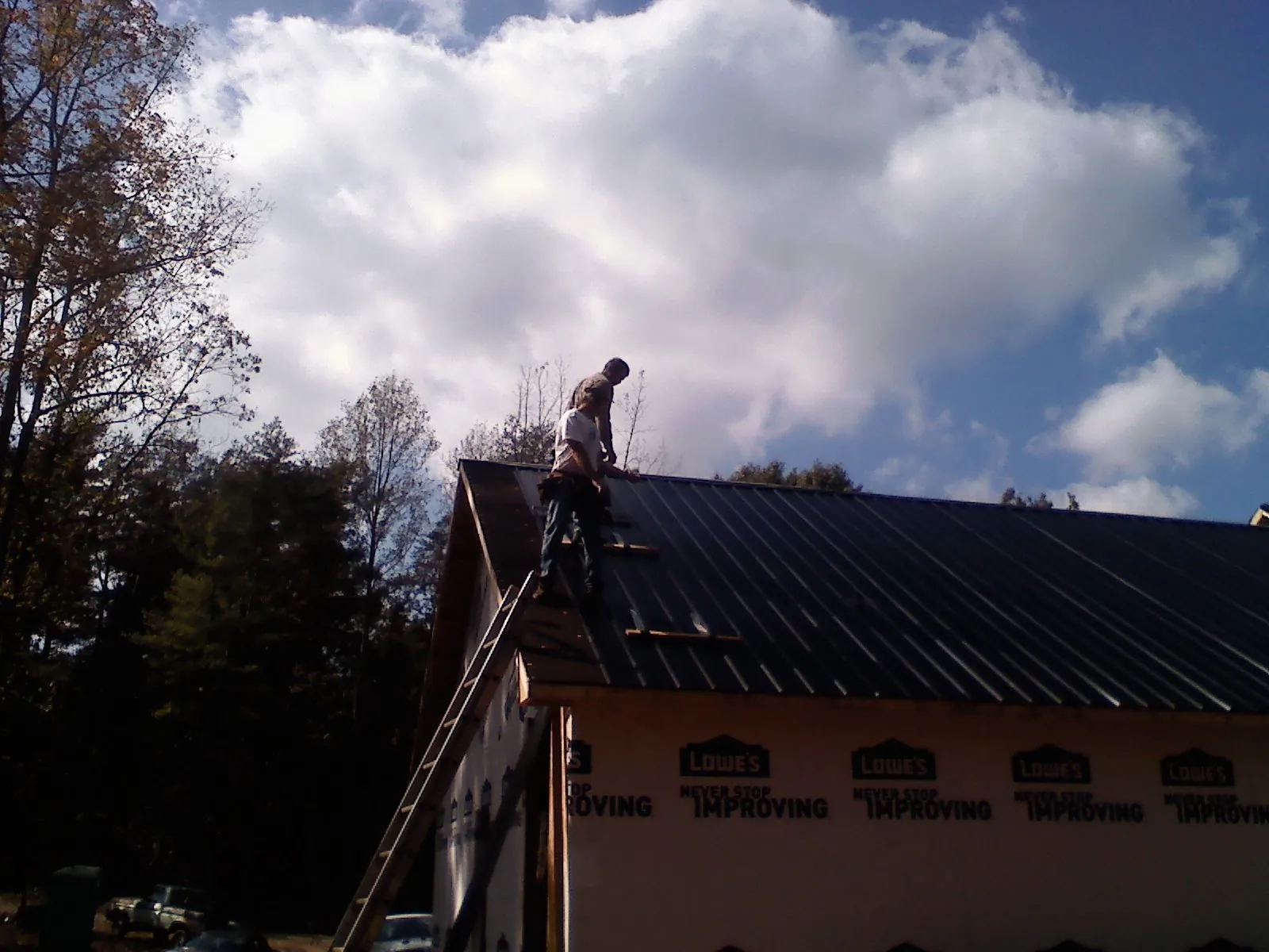 Roofer fastening dark metal panels high against a cloudy sky, from a Roof Inspection job in Slayden
