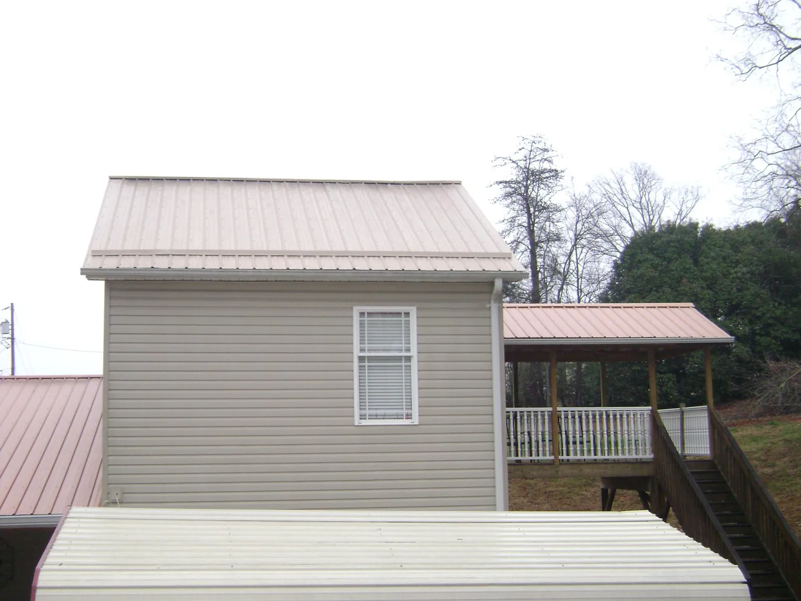 Tan metal roofs on a two story addition and attached porch, from a Roof Replacement job in Slayden